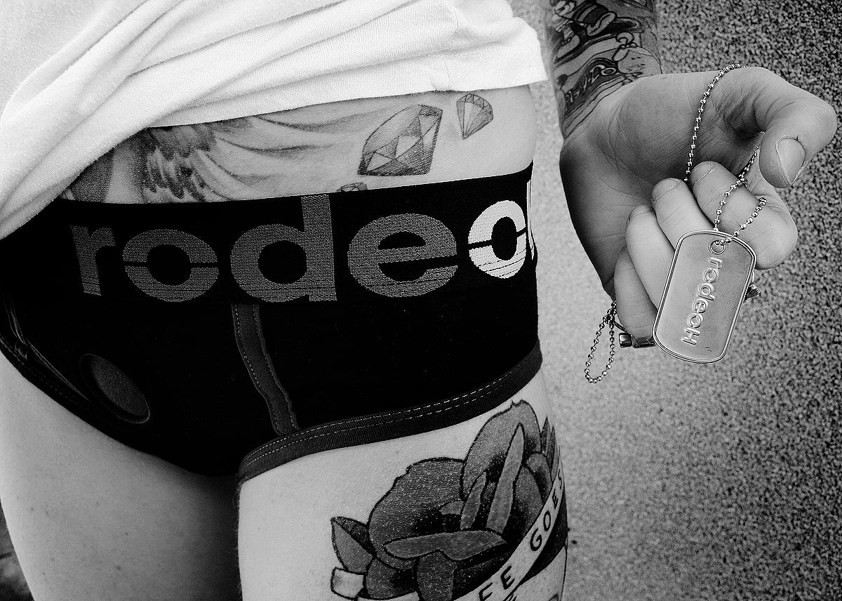 person wearing rodeoh brief harness and holding dog tag