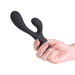 A matte black silicone dual-stimulation personal massager being held by a hand against a solid white background.