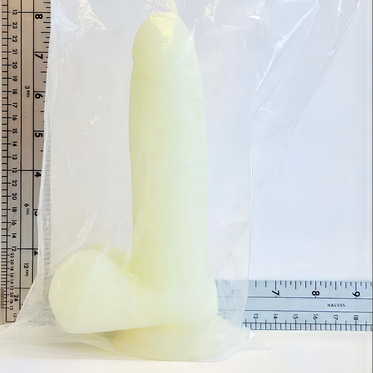glow in the dark silicone dildo with suction cup base in front of ruler showing dimensions