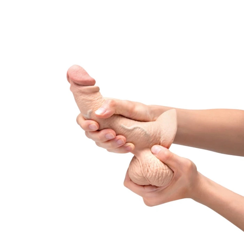 b Vibe Cream colored slip skin dildo,  in two hands to show flexibility and texture of balls