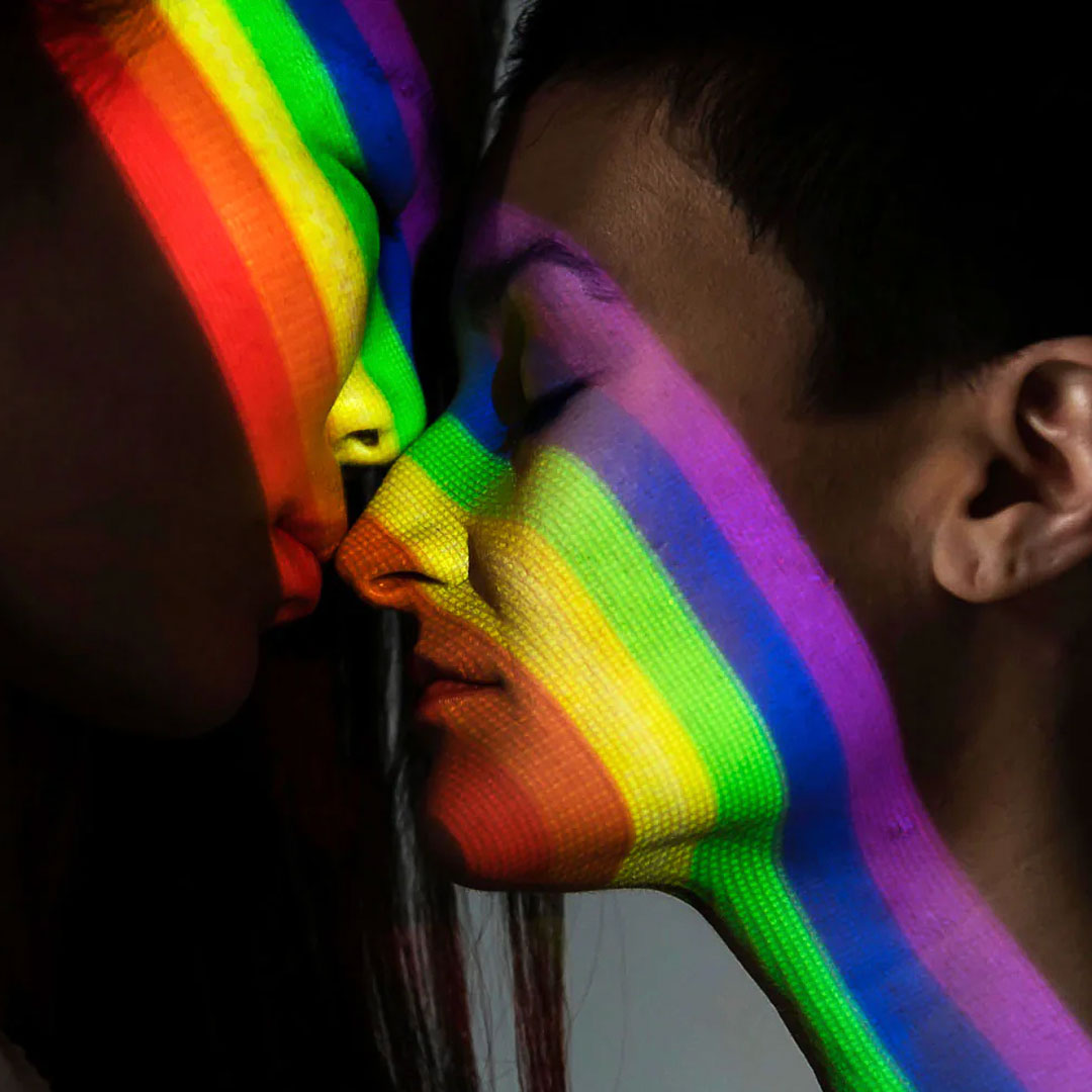 two people facing each other with pride rainbow cast across their faces