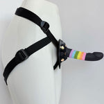 Nexus Fun and Love harness kit with adjustable black strap on harness and Rainbow Prysm tease silicone dildo, with dildo inserted into the harness and harness on a mannequin, angled from the side, with view of how the straps work around the back and side of body