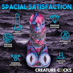 XR Brands Creature Cocks Alienoid Pink, black, blue and glitter silicone fantasy dildo with eye balls for testes from above, with graphic text of the features on a rocky backdrop